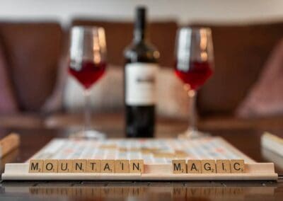 Mountain Magic Scrabble Tiles with two wine glasses and wine bottle in the blurry background